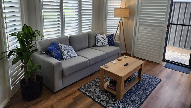 Una sala de estar con un sofá gris, cojines estampados, una mesa de centro de madera y una planta en maceta.
