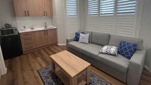 Un espacio habitable compacto con kitchenette, sofá gris con cojines estampados y una mesa de centro de madera.
