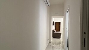 A hallway with a marble floor, white walls, and an air conditioning unit mounted on the wall.