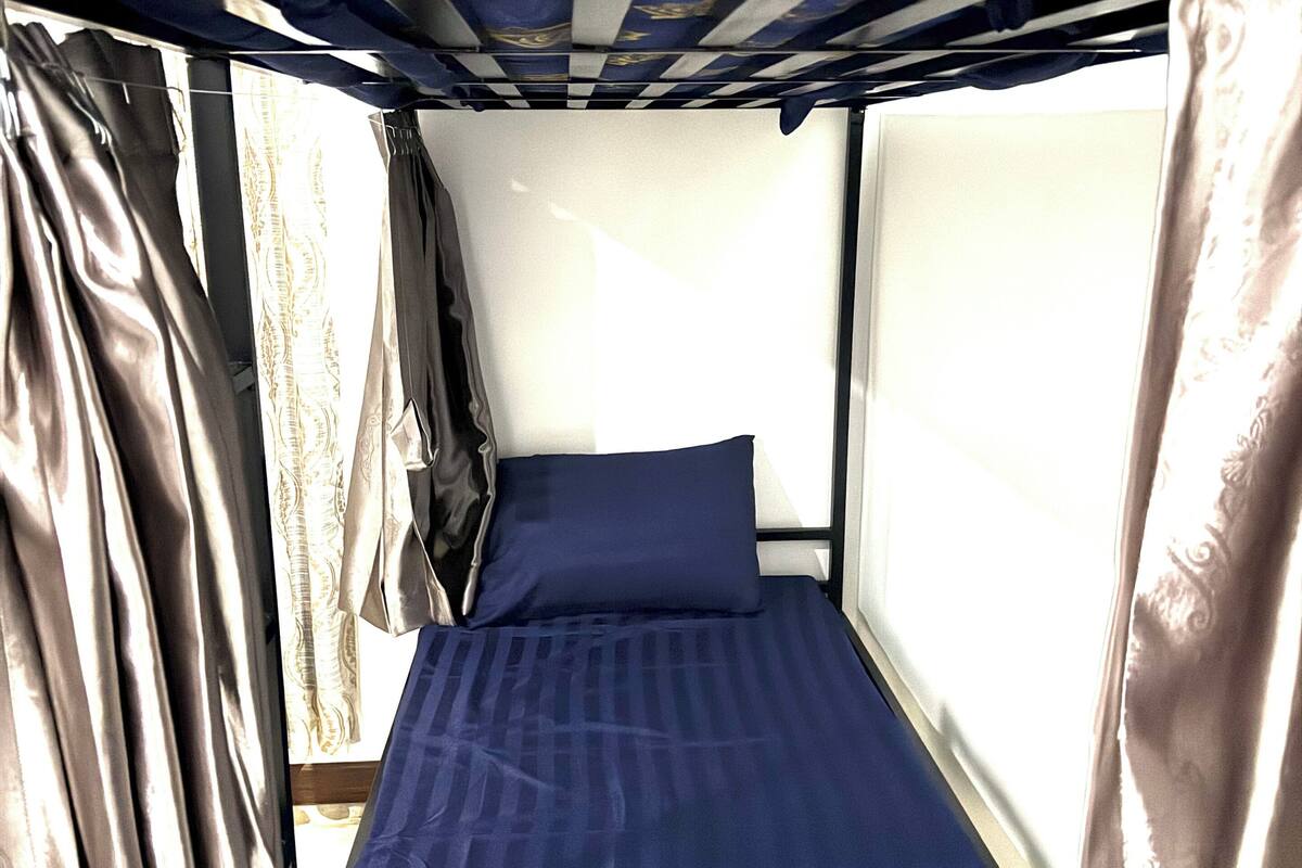 A bunk bed with a blue mattress and pillows, curtains, and a window.