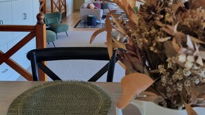 A modern living room with a sofa, a dining table with a woven placemat, and a vase with dried flowers. - Doug's Place - Spectacular Views + Tennis Court (Nindaroo)