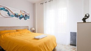 Un dormitorio con cama, lámpara, ventana con cortinas y refrigerador.