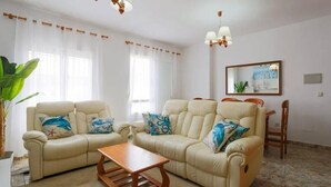 Un salón con dos sofás beige, una mesa de centro de madera y una zona de comedor con una silla y una mesa.