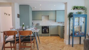 A modern kitchen with light blue cabinets, a dining area with wooden chairs, and a blue cabinet with glass doors. - 1 Mill Green Court (Lyme Regis)