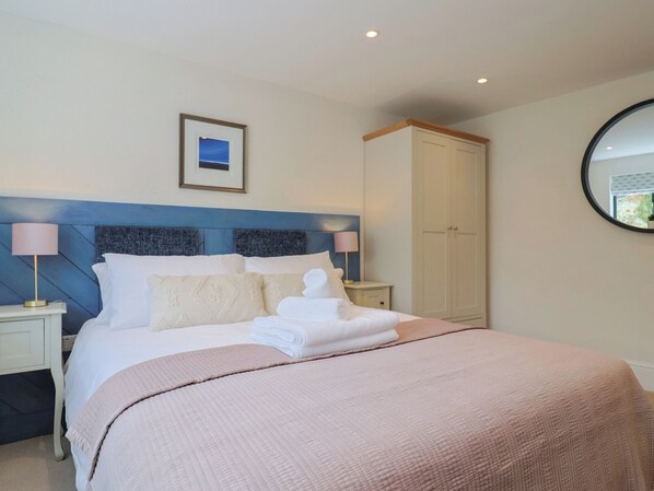 A neatly made bed with a pink blanket, two bedside lamps, a framed picture on the wall, and a wardrobe.