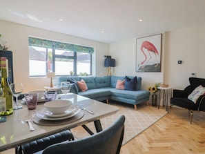 A modern living room with a sectional sofa, dining table with chairs, and a painting of a flamingo on the wall. - 1 Mill Green Court (Lyme Regis)
