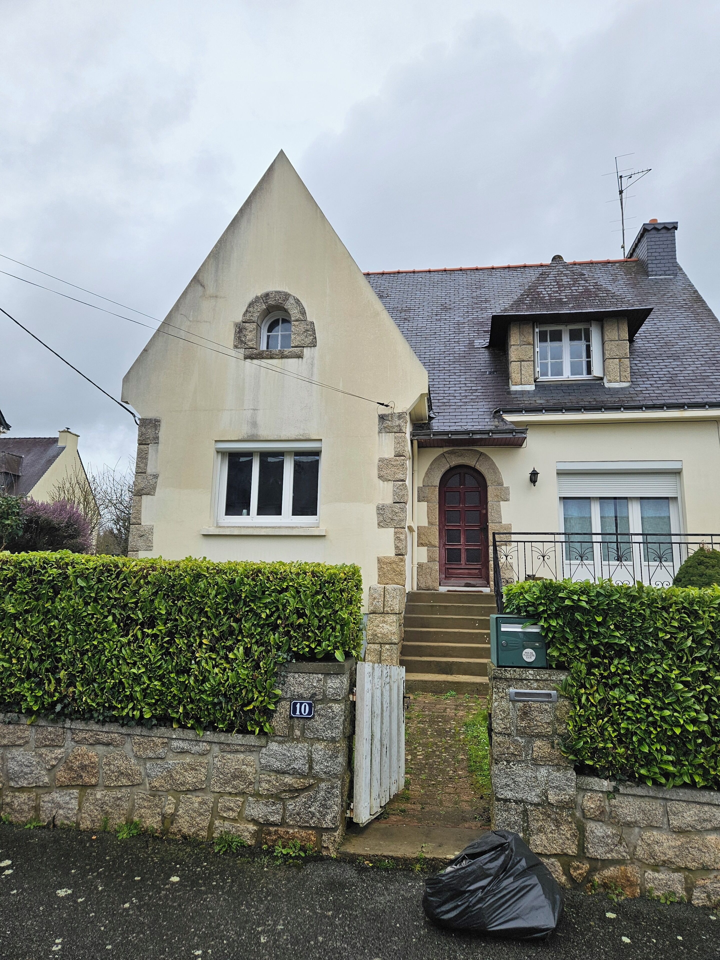 A two-story house with a stone facade, a red door, and a small front garden.