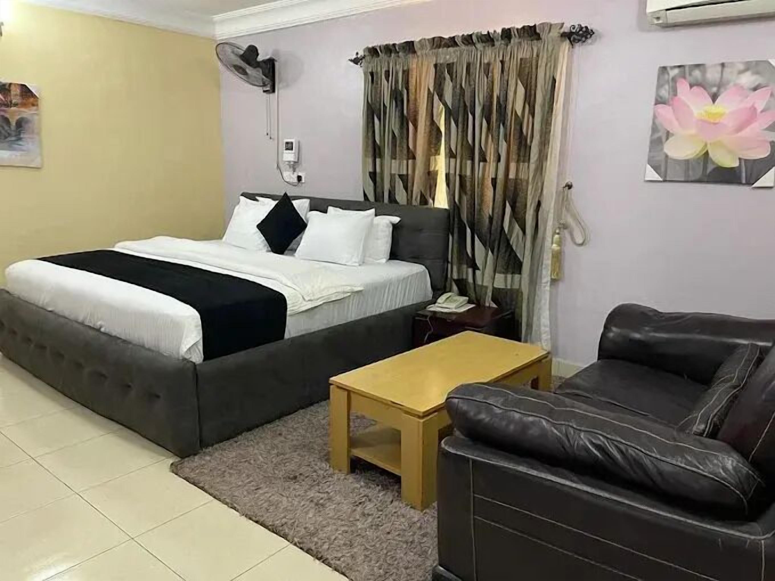 A bedroom with a bed, a nightstand, a table, a sofa, a fan, and curtains.