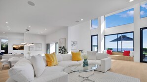 A spacious living room with a white sectional sofa, a glass coffee table, and large windows offering a view of the outdoors. - Morning View Malibu -Malibu Masterpiece in the Making w/ Views & Beach Access (Malibu)