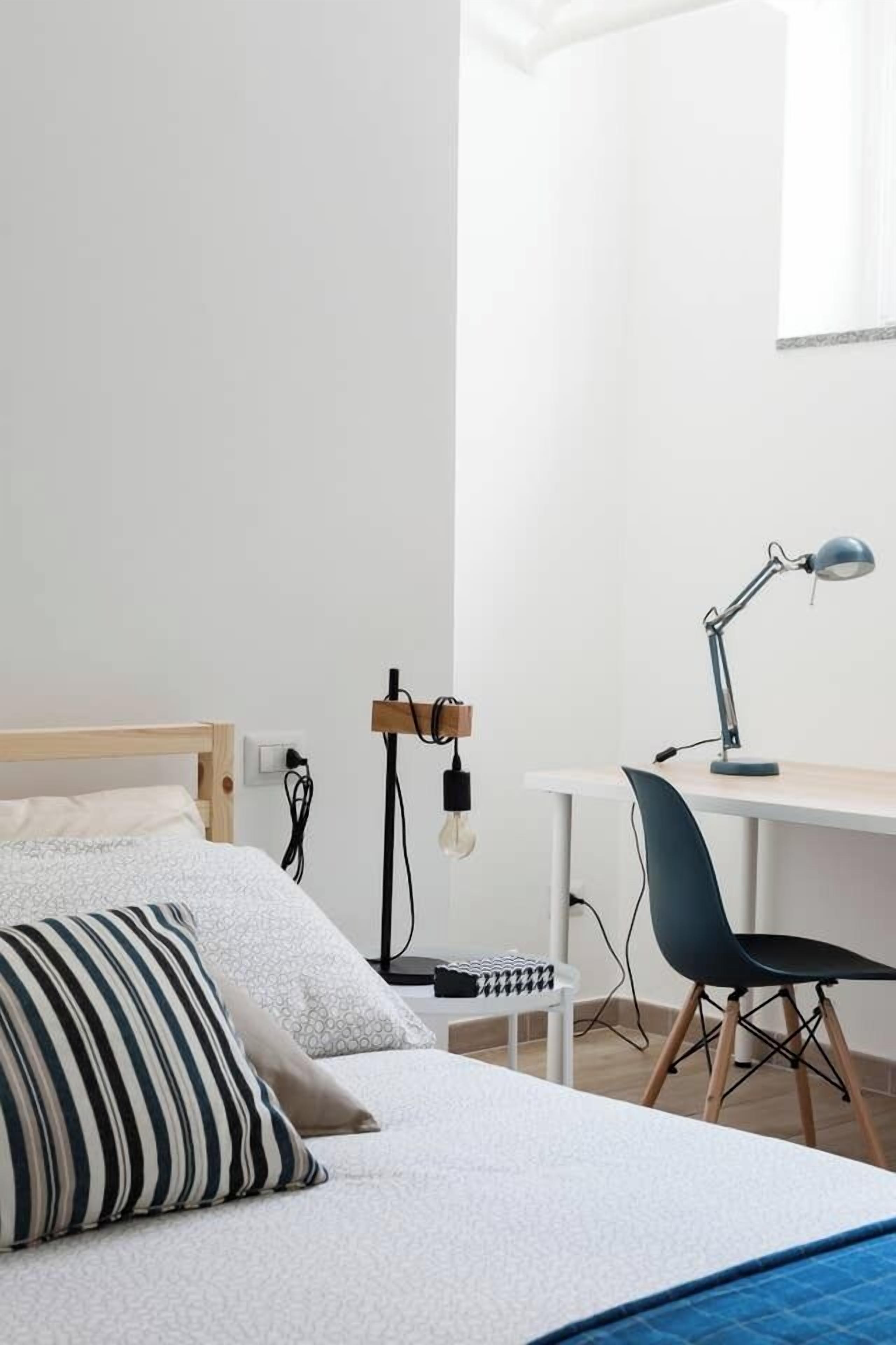 A bedroom with a bed, a desk, a chair, and a lamp.
