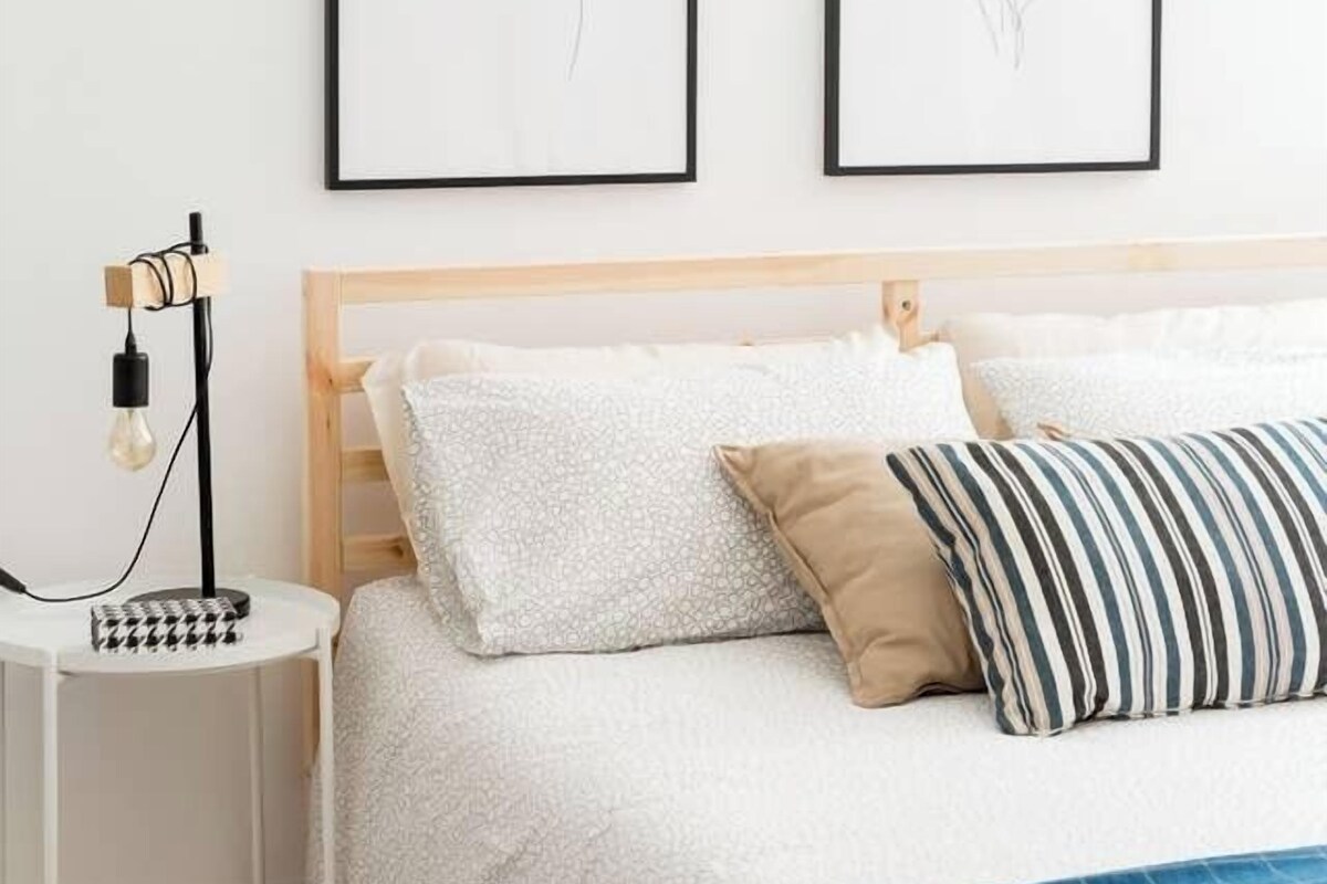 A bedroom with a wooden headboard, white bedding, and two framed line art pieces on the wall.