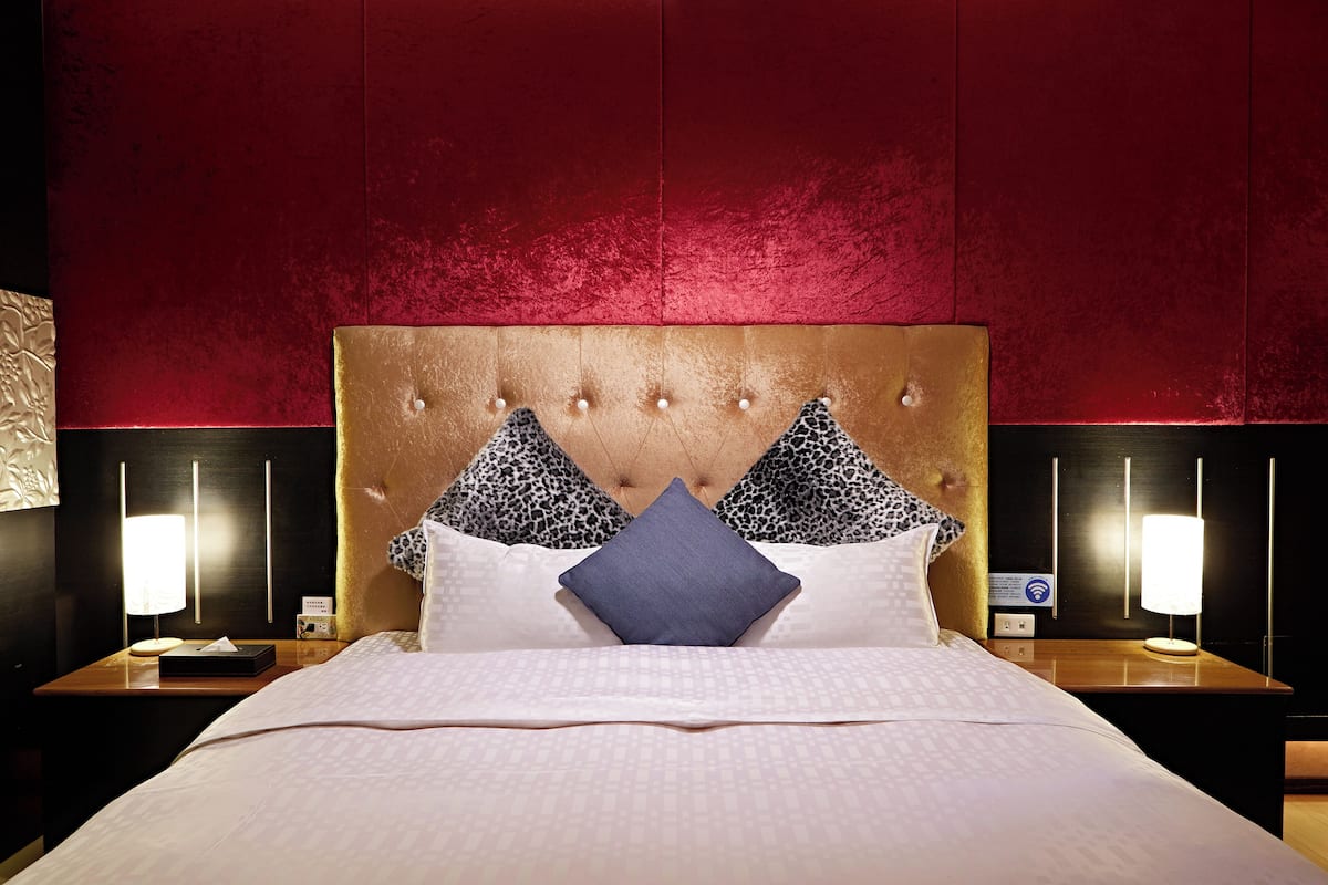 A hotel room with a tufted headboard, two bedside lamps, a nightstand, and a bed with patterned bedding.