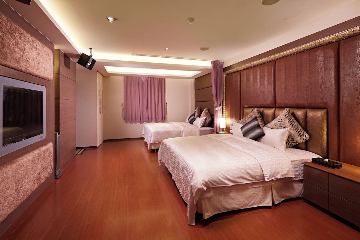 A hotel room with two beds, a flat-screen TV, a wooden floor, and a modern ceiling design.