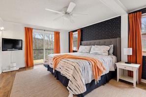 A bedroom with a bed, a ceiling fan, a TV, and a window with curtains.