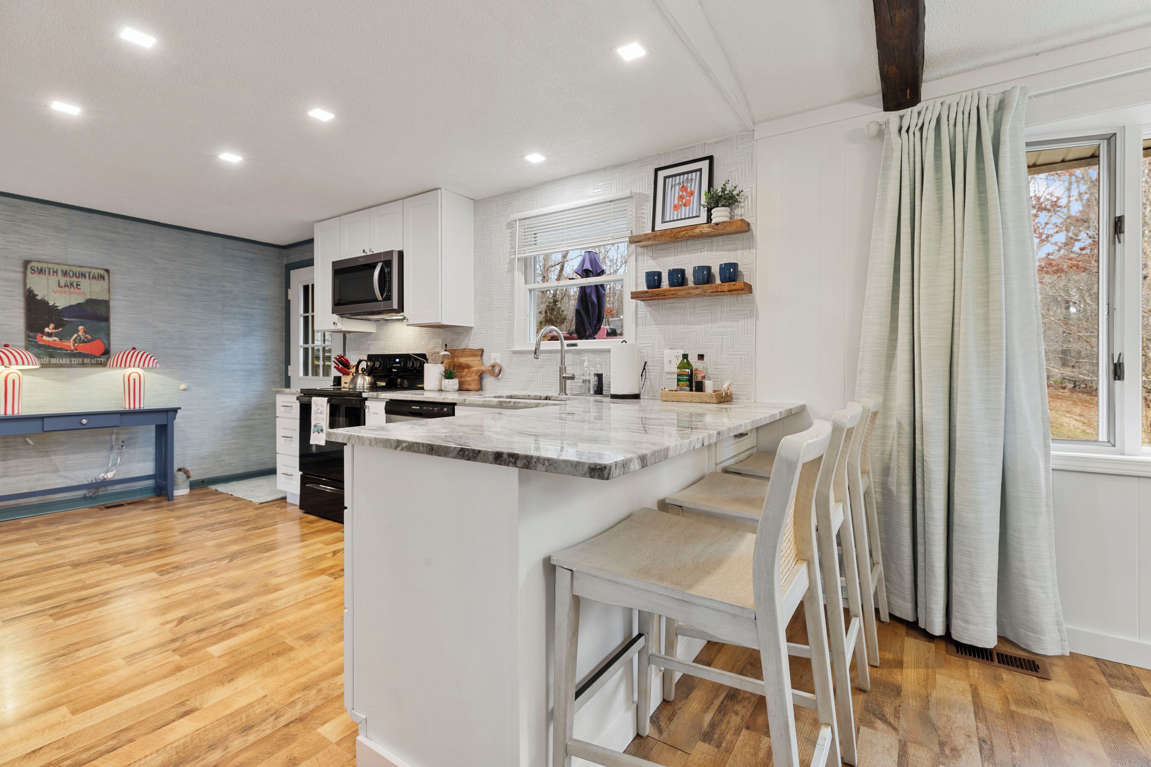 Een moderne keuken met een centraal eiland, houten vloeren en een raam met gordijnen.