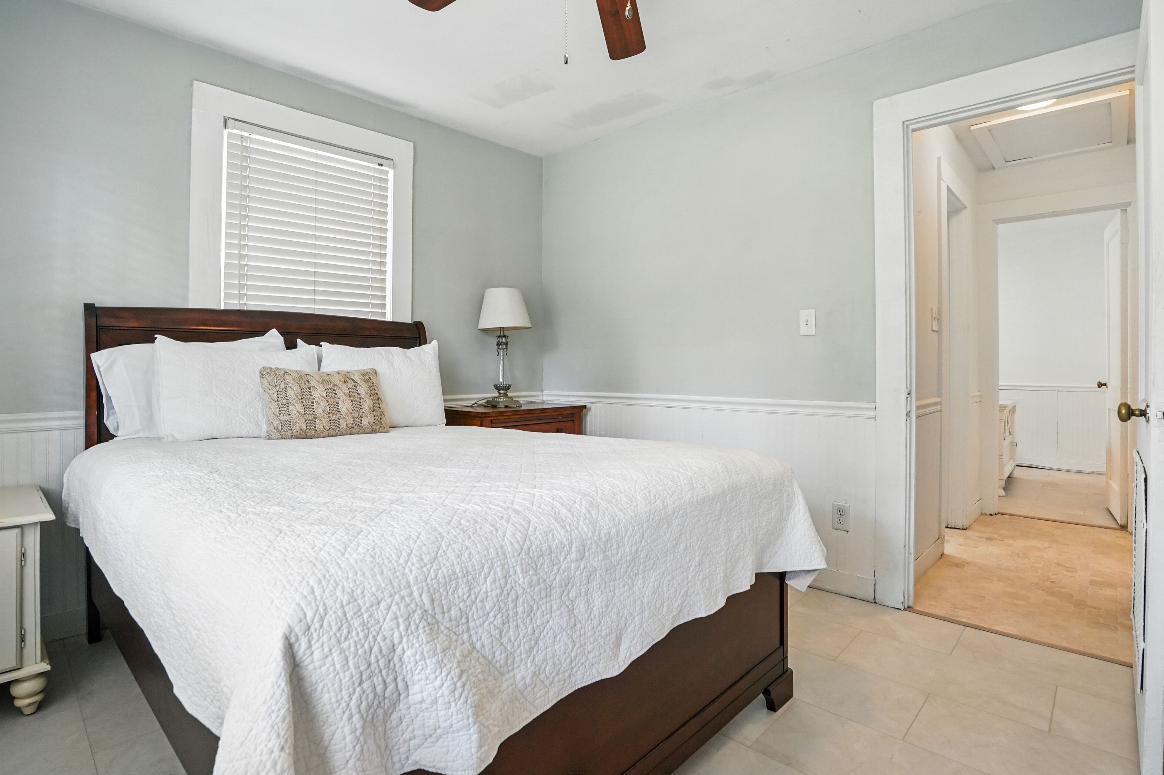 A bedroom with a large bed, a bedside table with a lamp, and a door leading to another room.