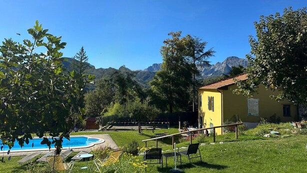 A pool area with lounge chairs, a yellow building, and mountains in the background. - Carina in Toscana, garden apartment with private pool in beautiful Garfagnana. (Colognola)