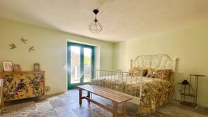 A bedroom with a bed, a bench, a dresser, a door, and a hanging light fixture. - Carina in Toscana, garden apartment with private pool in beautiful Garfagnana. (Colognola)