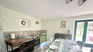 A kitchen with a wooden table, chairs, and a dining area. There is a refrigerator, oven, and sink. The walls have framed pictures and a clock. - Carina in Toscana, garden apartment with private pool in beautiful Garfagnana. (Colognola)