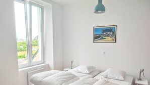 A bedroom with a bed, a bedside table, a lamp, a window, and a painting on the wall. - LANDES HOLIDAY HOME (Penmarch)