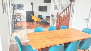 A dining area with a wooden table and blue chairs, a staircase, and a kitchen area with a stove and chairs. - LANDES HOLIDAY HOME (Penmarch)