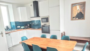 A modern kitchen with white cabinets, a wooden dining table, and teal chairs. - LANDES HOLIDAY HOME (Penmarch)