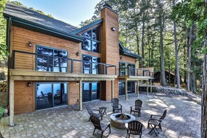 A modern two-story house with a wooden exterior, large windows, and a fire pit in the backyard. - New! Gorgeous lakeside luxury cabin on Laura Lake with dock, patio, and firepit! (Star Lake)