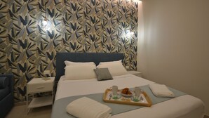A neatly made bed with a tray of breakfast items, a bedside table with a lamp, and a patterned wall.
