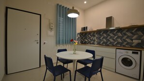 A compact kitchen with a washing machine, a dining table with chairs, and a blue curtain.