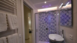 A modern bathroom with a glass shower enclosure, a white sink, and a towel rack with white towels.