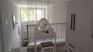 A room with a vanity, a mirror, and a window with sheer curtains.