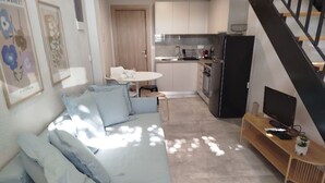 A living room with a sofa, a TV on a wooden stand, and a kitchen in the background.