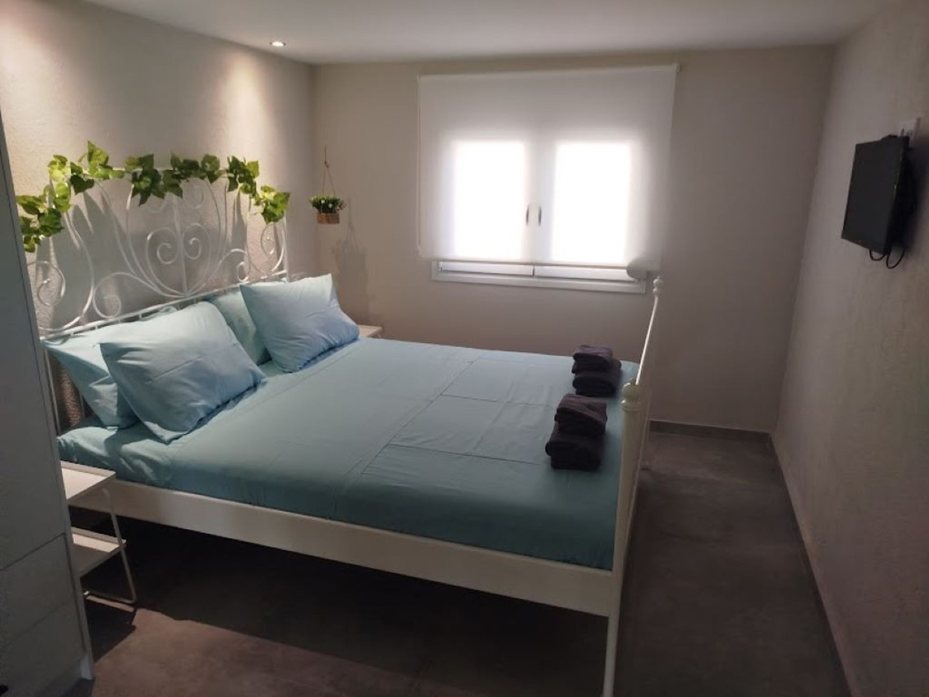 Een slaapkamer met een bed, een raam en een televisie aan de muur.