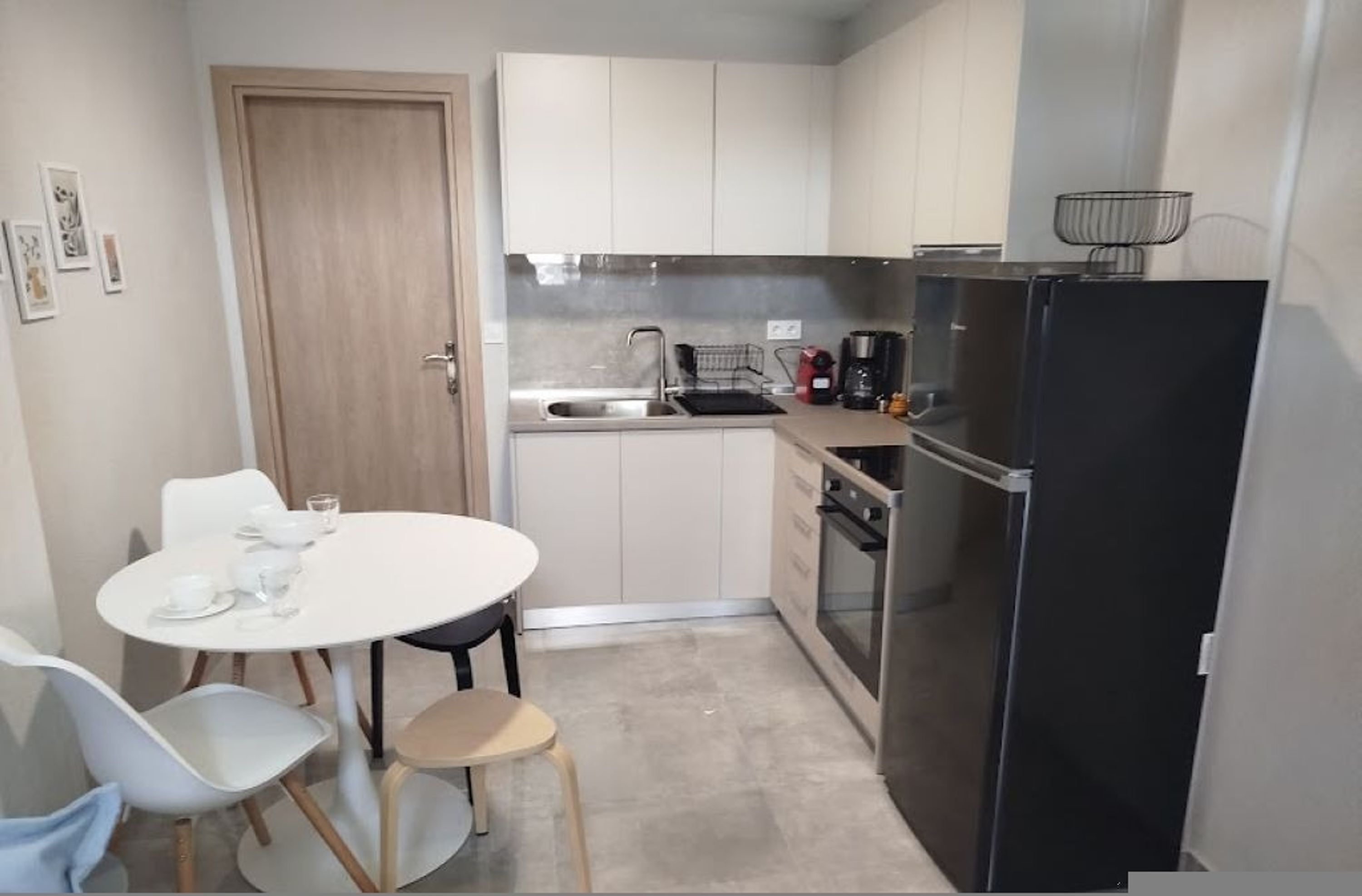 A compact kitchen with a sink, stove, and refrigerator, a small dining table with chairs, and light-colored cabinets.