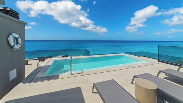 A rooftop pool with clear blue water, lounge chairs, and a lifebuoy on the wall.