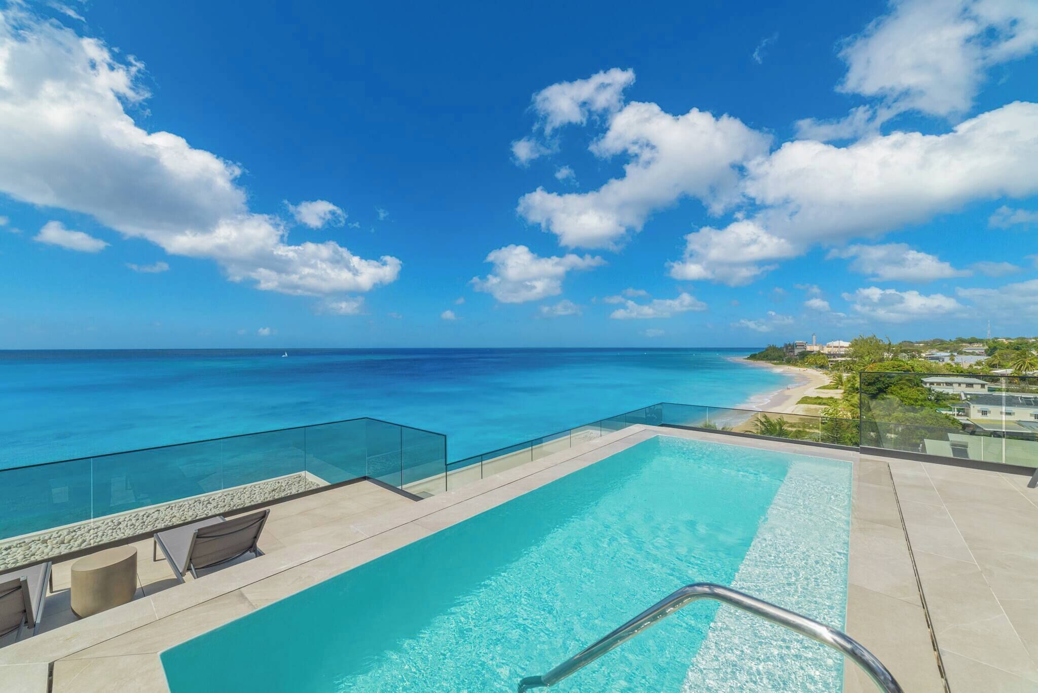 A rooftop infinity pool with clear blue water, overlooking a beach and ocean.