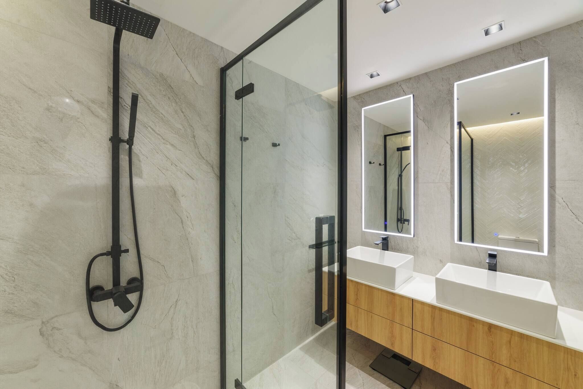 A modern bathroom with a glass-enclosed shower, two sinks with mirrors, and a wooden vanity.