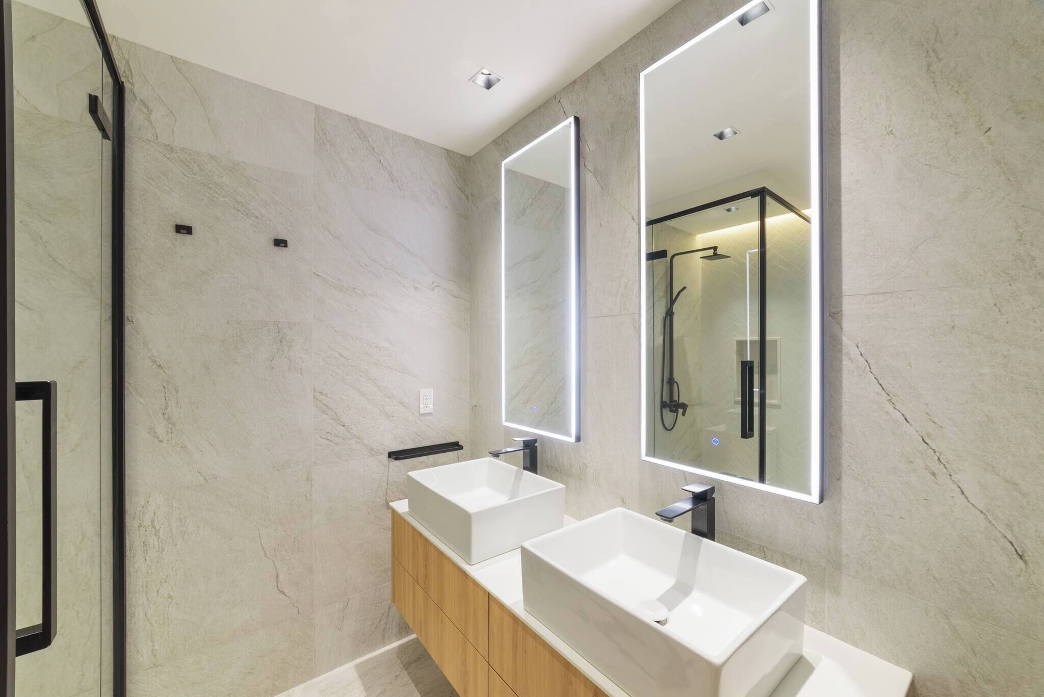 A modern bathroom with two large white sinks, a wooden vanity, and a glass shower enclosure.