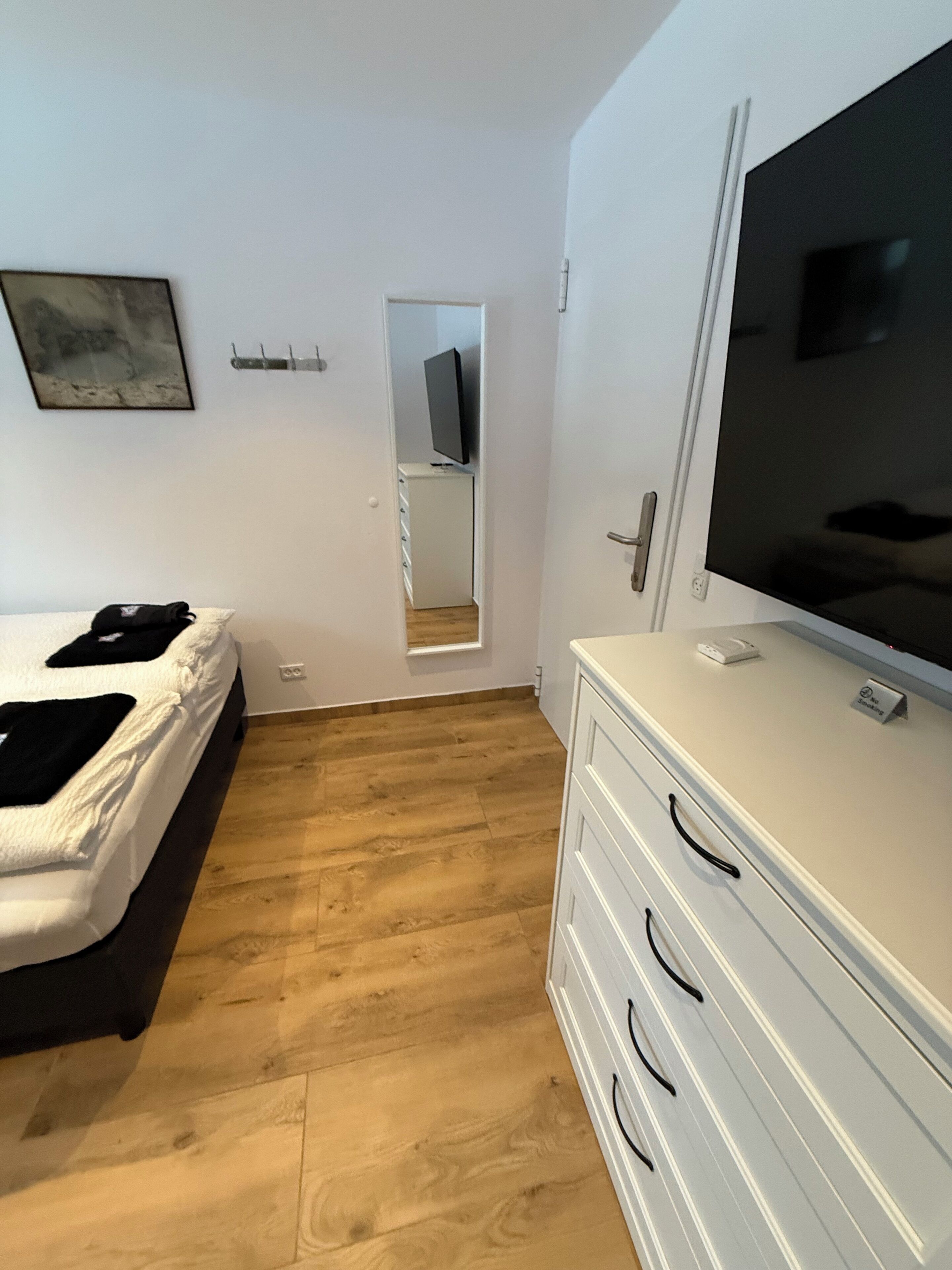 A bedroom with a bed, a dresser, a TV, and a mirror.