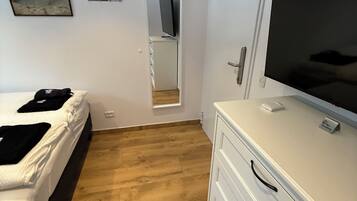 A bedroom with a bed, a dresser, a TV, and a mirror.