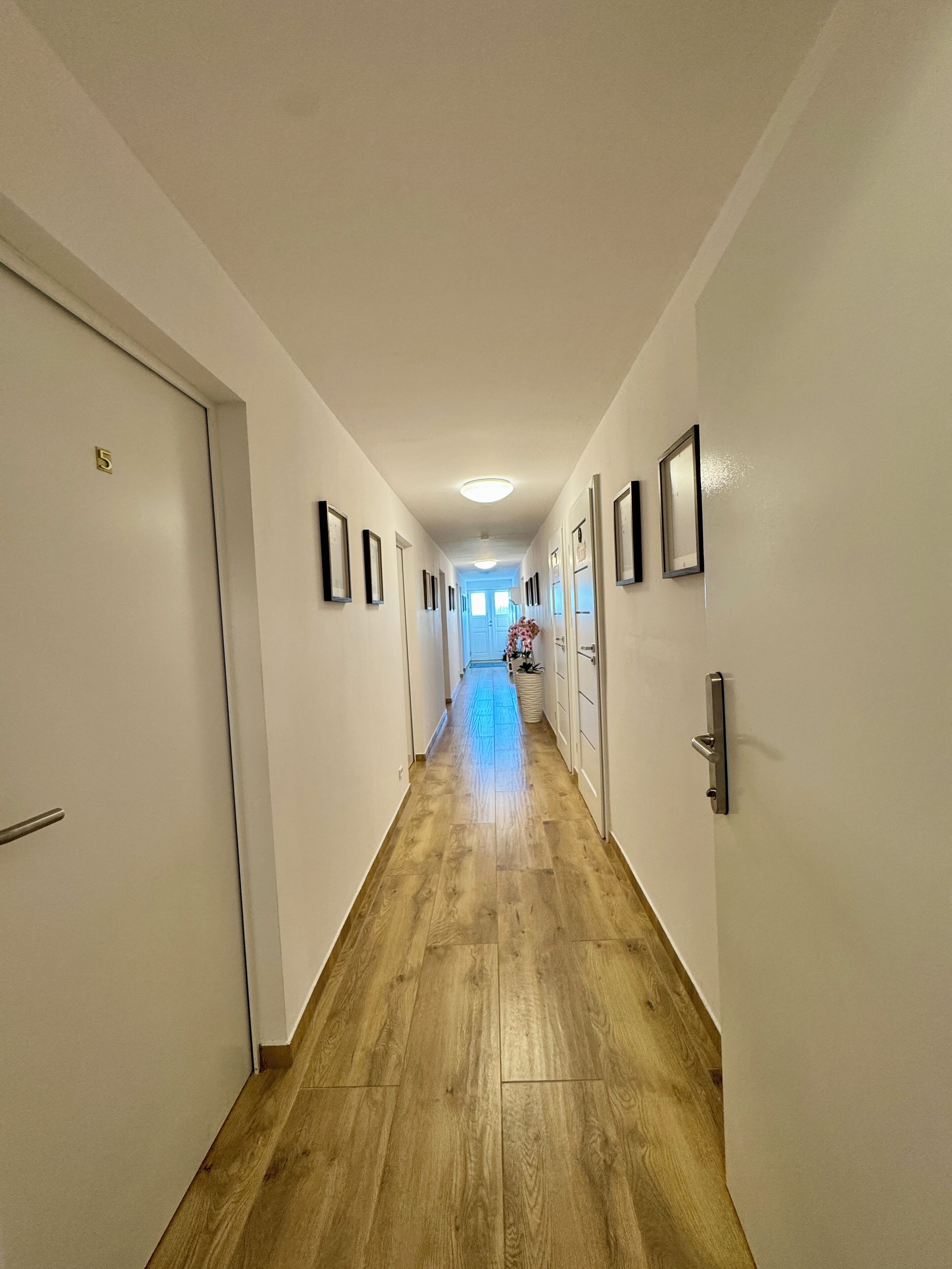 A hallway with wooden flooring, white walls, and doors numbered 5.