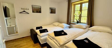 A hotel room with two beds, a wooden floor, a window with curtains, and a mirror.