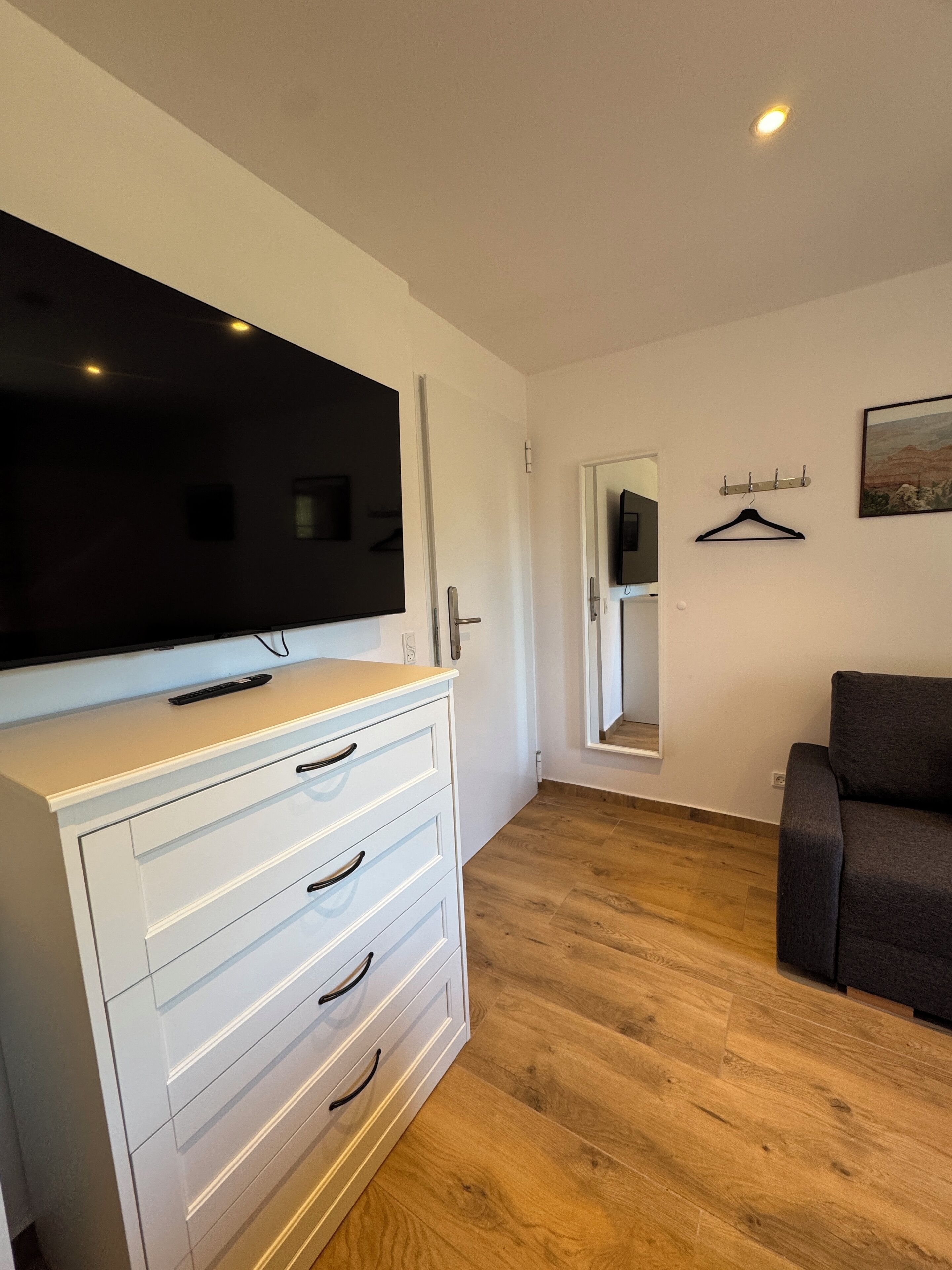 A modern living room with a flat-screen TV on a white cabinet, a grey sofa, and a wooden floor.