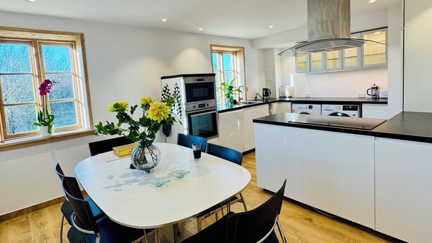 A modern kitchen with white cabinetry, a central island, and a dining area with a round table and chairs. - Casa de Rainer Tommerup (Tommerup)