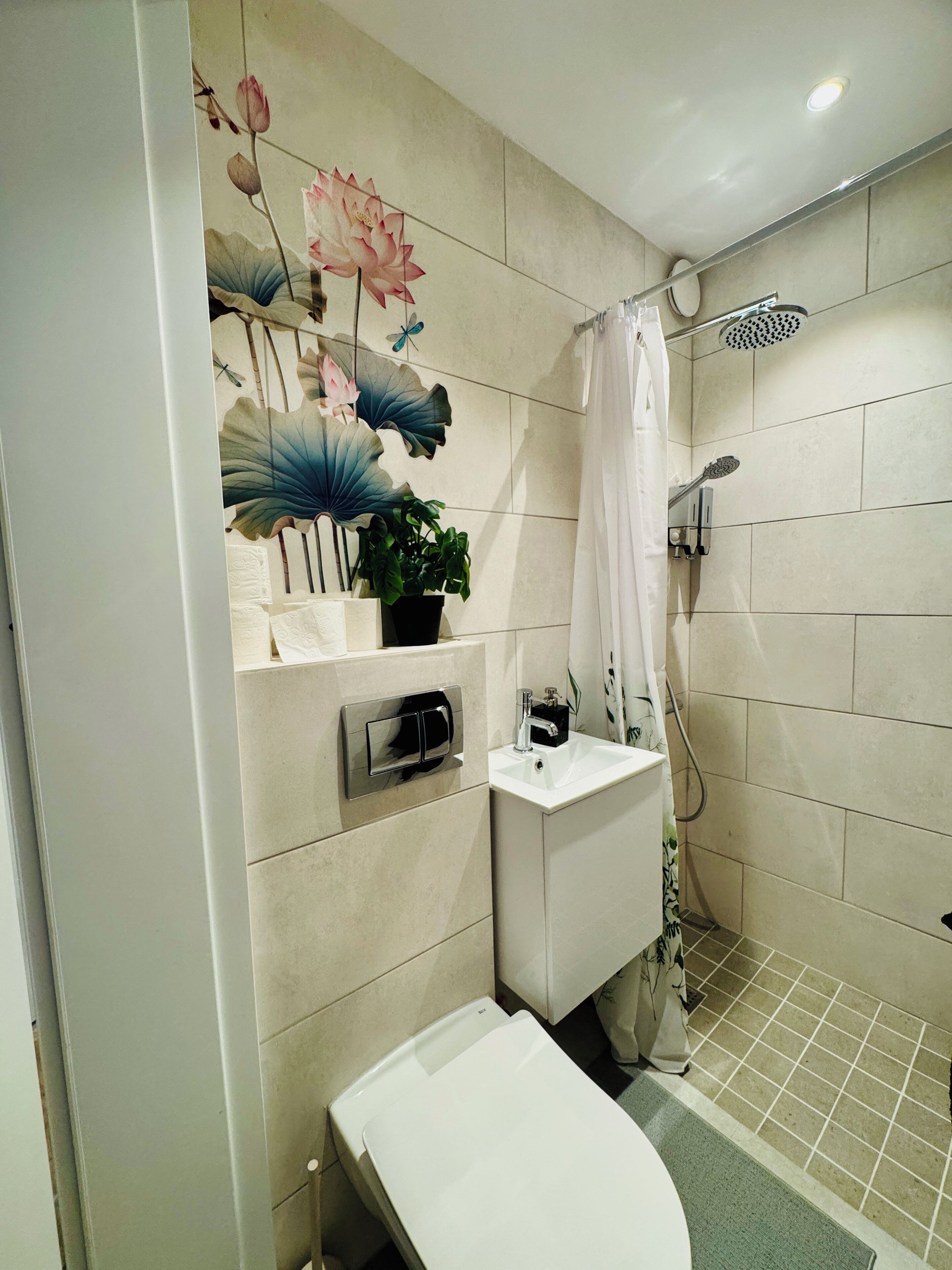A modern bathroom with a toilet, sink, and shower. There is a decorative wall with lotus flowers and a butterfly.