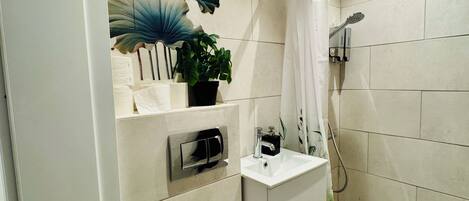 A modern bathroom with a toilet, sink, and shower. There is a decorative wall with lotus flowers and a butterfly.