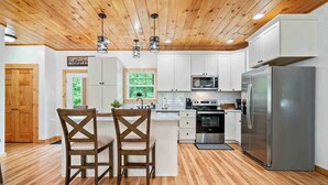 Une cuisine moderne avec un plancher en bois, des armoires blanches, des appareils électroménagers en acier inoxydable et un îlot central doté de deux chaises.