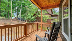 Une terrasse en bois avec une rambarde, un banc et une vue sur un chalet situé dans une zone boisée.