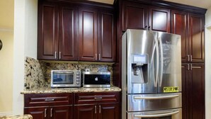 Una cocina con armarios de madera oscura, un refrigerador de acero inoxidable, un microondas y una cafetera.