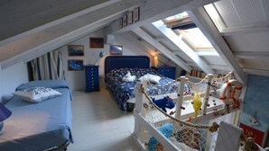 A bedroom with a sloped ceiling, a bed with a blue headboard, a small desk, and a birdcage with toys. - Cozy villa in a quiet area surrounded by nature of Lignano (Ente di decentramento regionale di Udine)